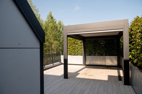 A sleek pergola on a wooden deck, surrounded by trees and clear skies